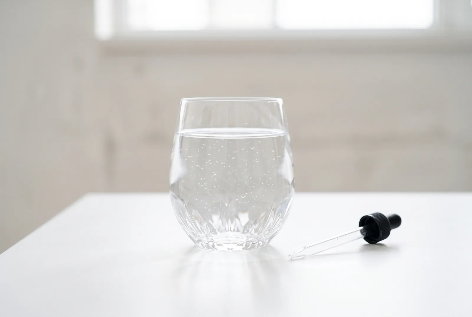A glass of clear water beside a laboratory dropper, tested for invisible contaminants